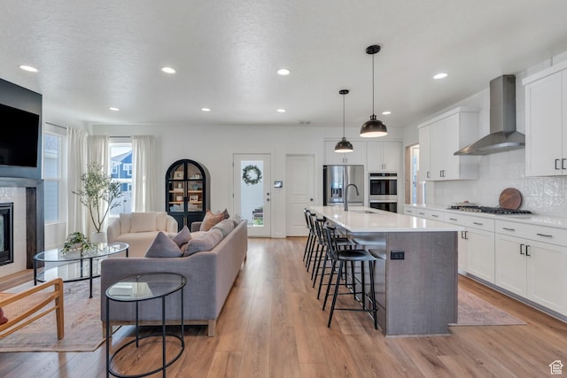 kitchen featuring wall chimney exhaust hood, a kitchen bar, appliances with stainless steel finishes, light countertops, and open floor plan