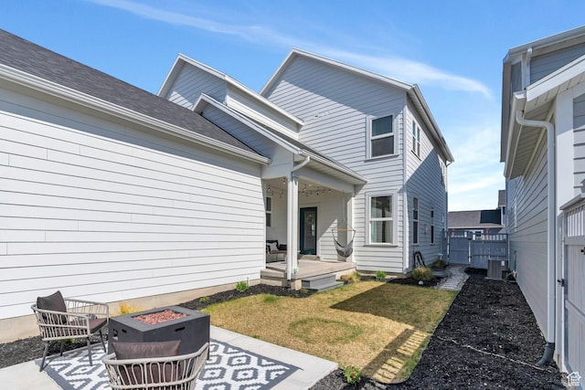 rear view of property featuring central AC unit, an outdoor fire pit, a lawn, a patio, and a gate