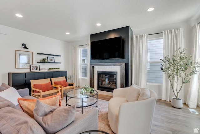 living room with a glass covered fireplace, recessed lighting, light wood finished floors, and visible vents