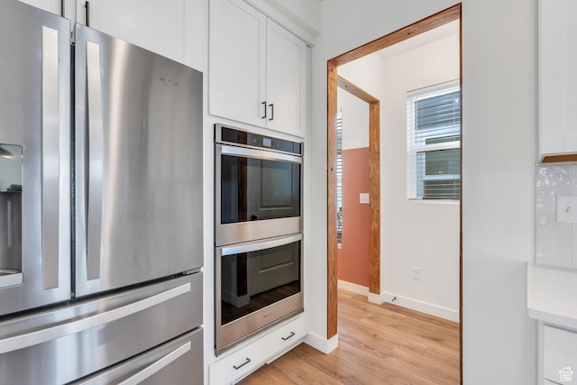 kitchen with light wood-style flooring, white cabinetry, light countertops, stainless steel appliances, and baseboards