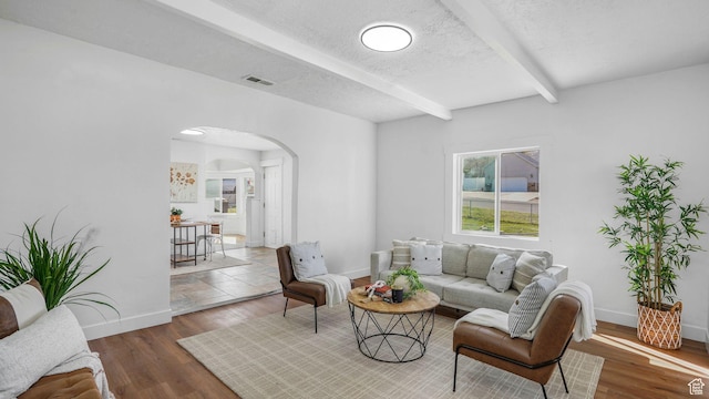 living area with beamed ceiling, arched walkways, visible vents, wood finished floors, and baseboards