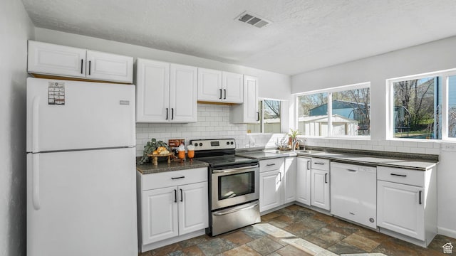 kitchen with visible vents, dark countertops, white appliances, white cabinetry, and backsplash