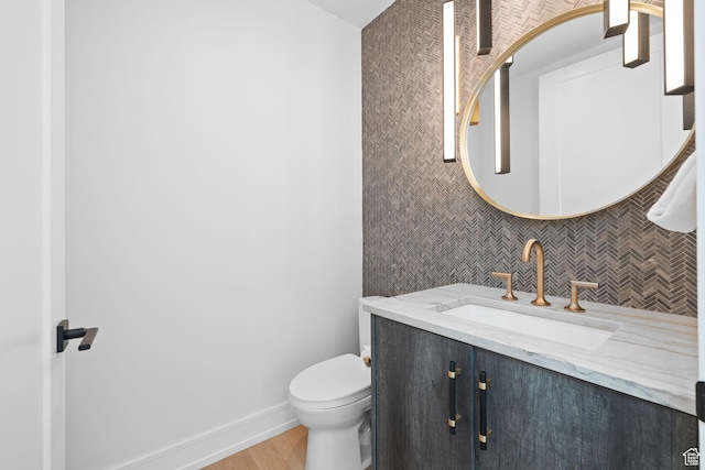 half bathroom featuring toilet, wood finished floors, vanity, and backsplash