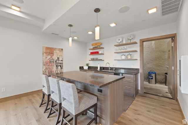 kitchen featuring a kitchen bar, open shelves, visible vents, a center island, and a sink