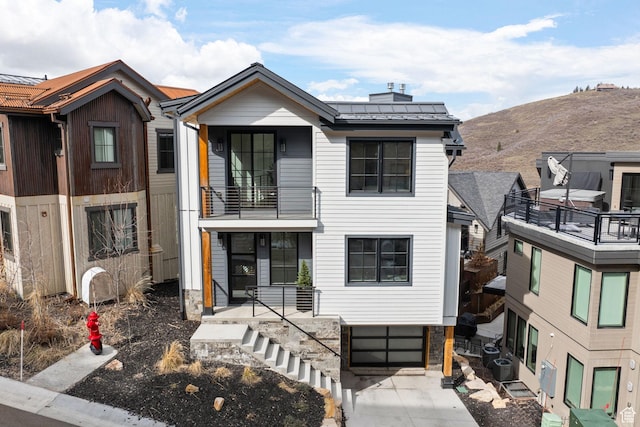 view of property featuring metal roof, a balcony, an attached garage, a chimney, and driveway