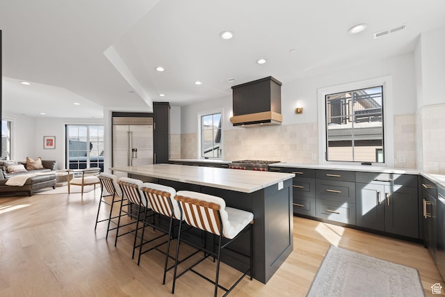 kitchen featuring custom range hood, built in refrigerator, a center island, and light wood-type flooring