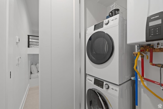 clothes washing area with stacked washing maching and dryer, laundry area, baseboards, and water heater