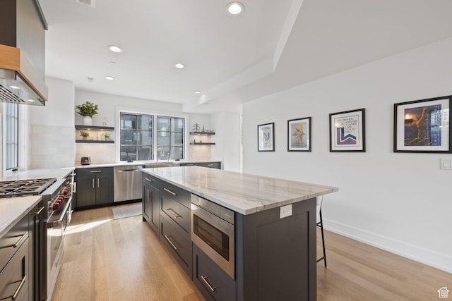 kitchen with open shelves, a kitchen island, light wood-style floors, wall chimney exhaust hood, and stainless steel appliances