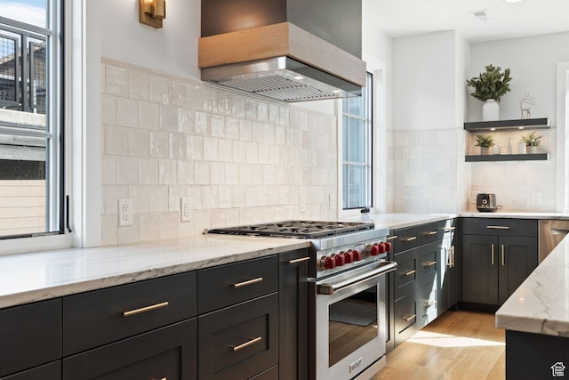 kitchen featuring luxury stove, light wood-style floors, light stone countertops, open shelves, and premium range hood