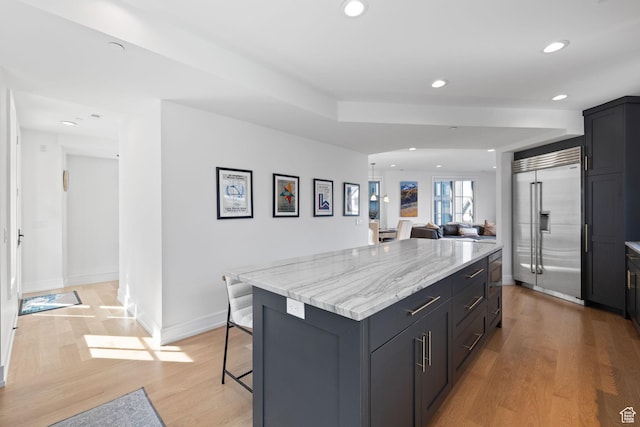 kitchen with built in fridge, recessed lighting, light wood finished floors, a kitchen island, and a breakfast bar area