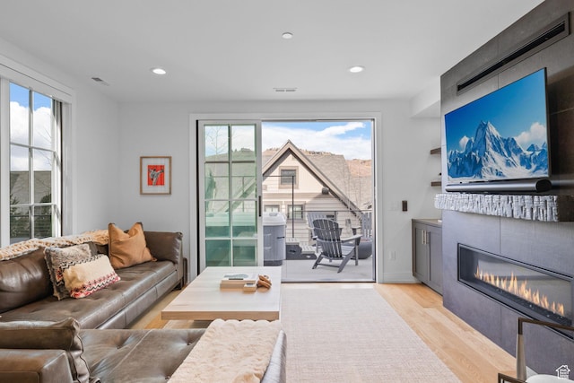 living room with light wood-type flooring, a healthy amount of sunlight, a glass covered fireplace, and recessed lighting