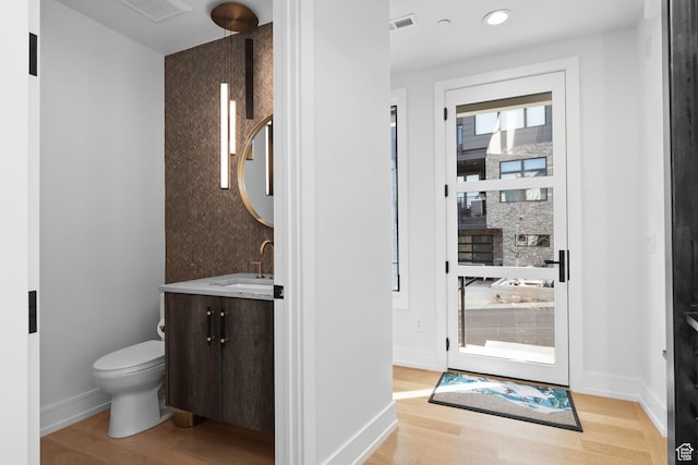 interior space with visible vents, baseboards, toilet, vanity, and wood finished floors