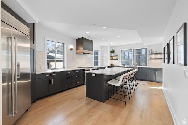 kitchen with custom range hood, a kitchen breakfast bar, backsplash, stainless steel built in refrigerator, and open shelves
