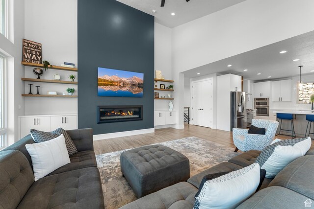 3131 E Lindsay Spring Rd, Heber City, UT 84032 - living room with ceiling fan, recessed lighting, a towering ceiling, light wood-style flooring, and a glass covered fireplace