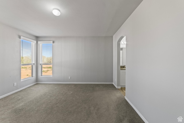 carpeted spare room featuring baseboards and arched walkways