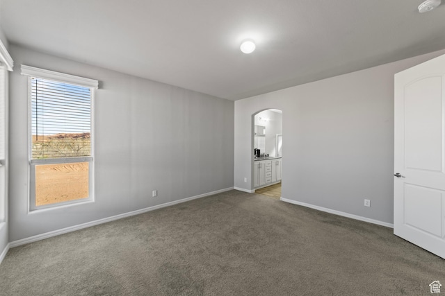 carpeted empty room with arched walkways and baseboards