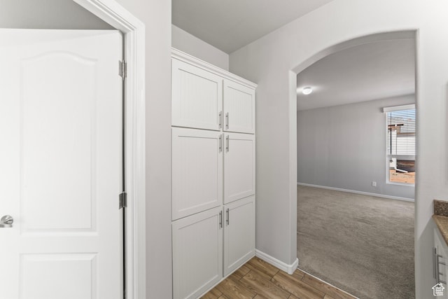 corridor with baseboards, arched walkways, light wood-style flooring, and light colored carpet