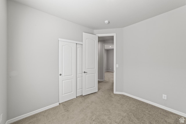 unfurnished bedroom featuring baseboards, light colored carpet, and a closet