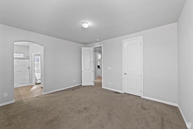 unfurnished bedroom with arched walkways, baseboards, carpet, and connected bathroom