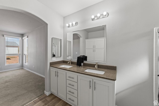 full bath featuring double vanity, baseboards, a sink, and wood finished floors