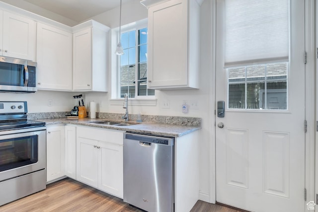 kitchen featuring light wood-type flooring, white cabinetry, light stone countertops, appliances with stainless steel finishes, and a sink