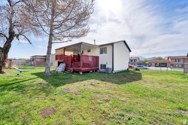 rear view of house featuring a wooden deck, fence, and a lawn