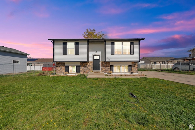 split foyer home featuring entry steps, stone siding, fence, concrete driveway, and a front lawn