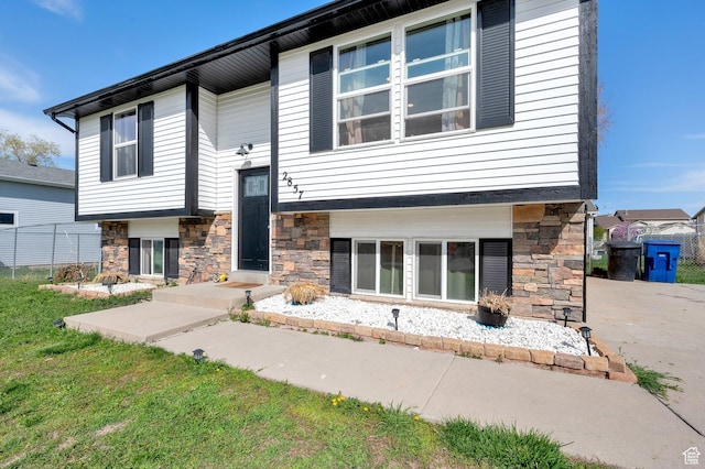 view of front of home with a front yard, stone siding, and fence