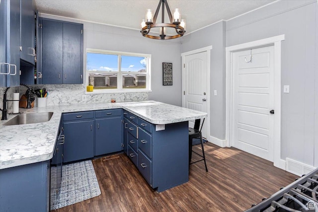 kitchen featuring a notable chandelier, a peninsula, blue cabinetry, dark wood finished floors, and a sink