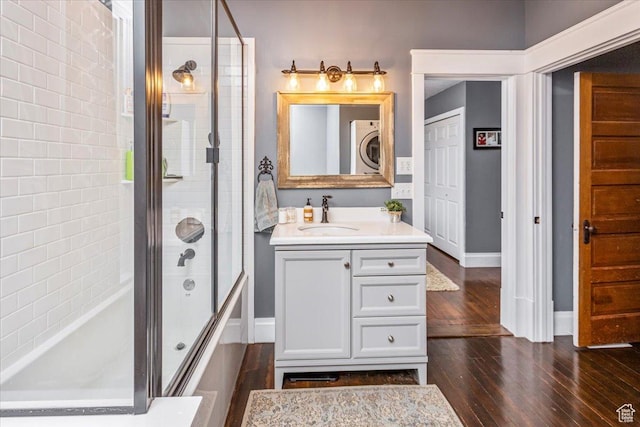 full bath featuring vanity, hardwood / wood-style floors, enclosed tub / shower combo, stacked washing maching and dryer, and baseboards