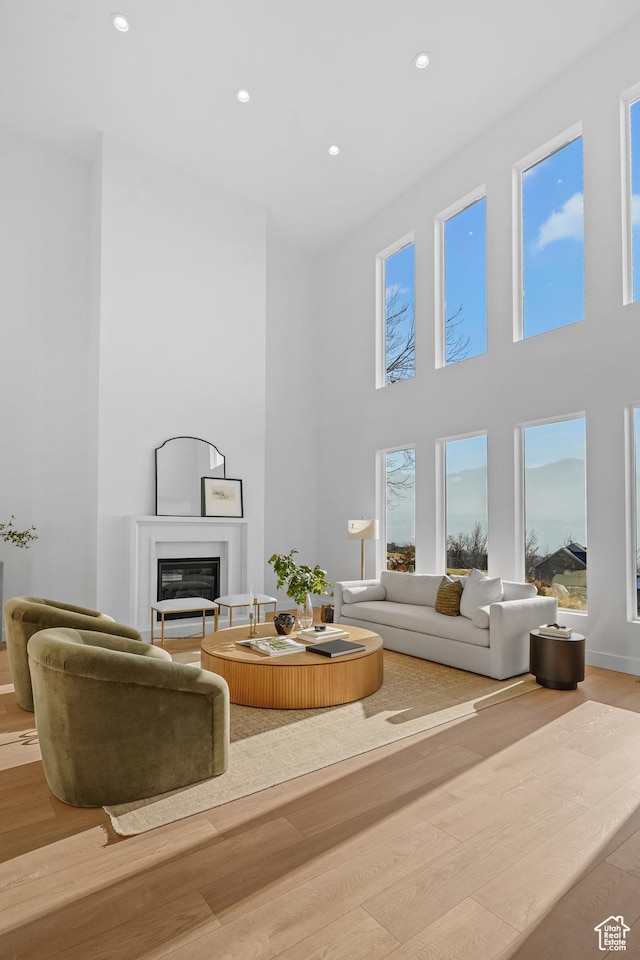 living area with a glass covered fireplace, recessed lighting, a high ceiling, and wood finished floors
