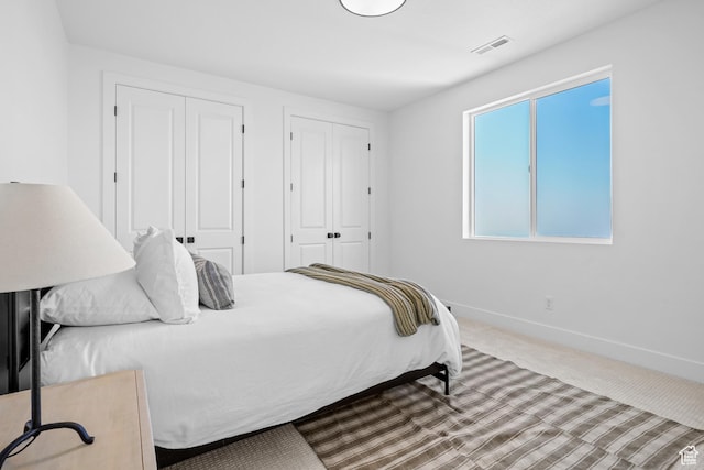 bedroom featuring carpet flooring, baseboards, visible vents, and multiple closets