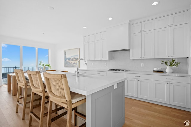 kitchen with premium range hood, white gas stovetop, a breakfast bar area, light wood finished floors, and a sink