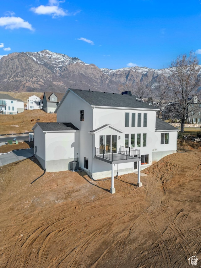 rear view of house featuring a mountain view, roof with shingles, and stucco siding