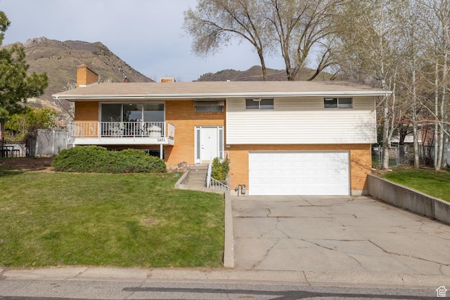 raised ranch featuring a mountain view, a front lawn, an attached garage, a chimney, and driveway