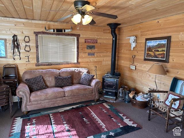 carpeted living area with a wood stove, wooden walls, wooden ceiling, and a ceiling fan