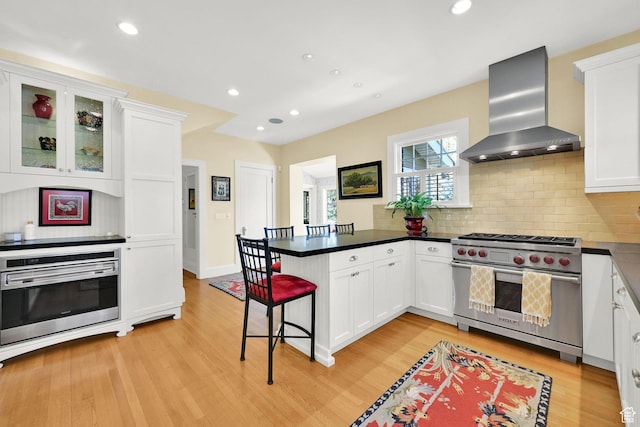 1401 E Sigsbee Ave, Salt Lake City, UT 84103 - kitchen with light wood finished floors, a peninsula, wall chimney exhaust hood, and appliances with stainless steel finishes