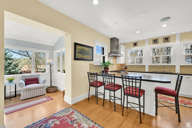 1401 E Sigsbee Ave, Salt Lake City, UT 84103 - kitchen featuring a kitchen breakfast bar, wall chimney range hood, dark countertops, light wood finished floors, and a baseboard radiator