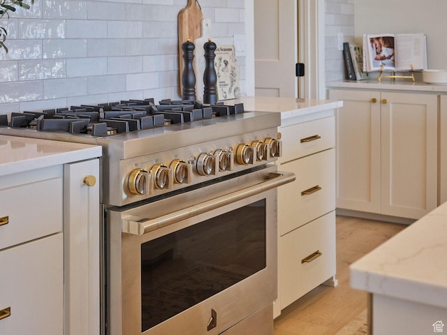 room details with white cabinets, light wood-style floors, decorative backsplash, and high end stove