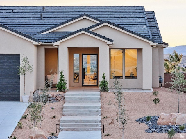 view of exterior entry with a garage, stucco siding, and driveway
