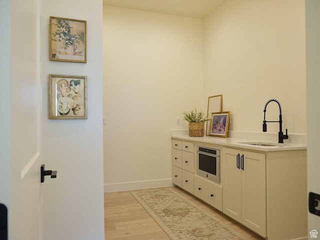 kitchen featuring baseboards, oven, a sink, light countertops, and light wood-type flooring