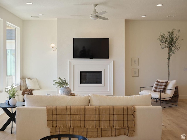 living area with a ceiling fan, light wood-style floors, a glass covered fireplace, and recessed lighting
