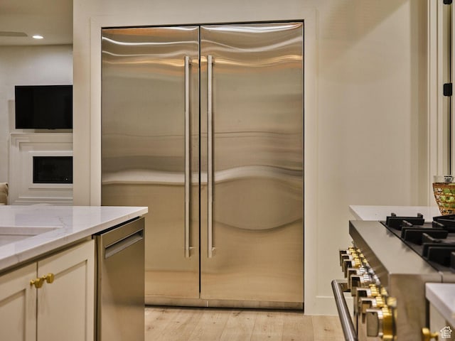 kitchen featuring light wood-type flooring, recessed lighting, light stone countertops, cream cabinets, and stainless steel appliances