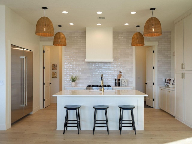 kitchen featuring tasteful backsplash, a breakfast bar, high end fridge, wall chimney range hood, and light wood finished floors