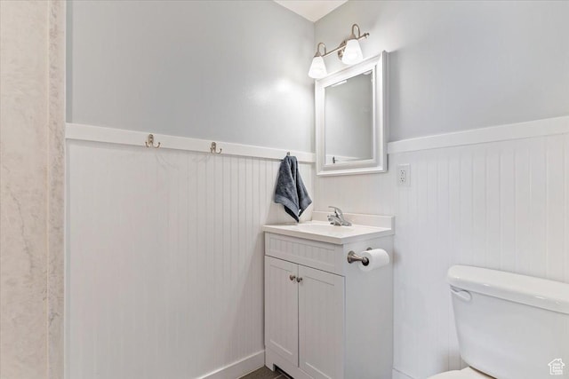 bathroom with toilet, vanity, and a wainscoted wall