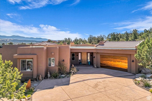 pueblo-style house with a garage, stucco siding, a tile roof, a mountain view, and concrete driveway