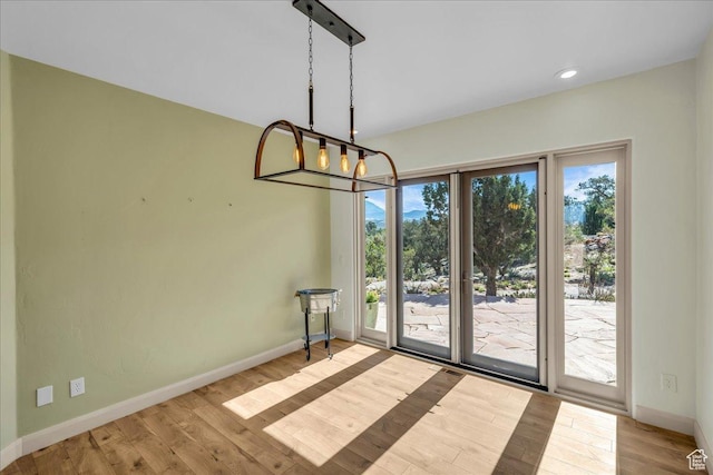 unfurnished dining area with wood finished floors, an inviting chandelier, baseboards, and recessed lighting