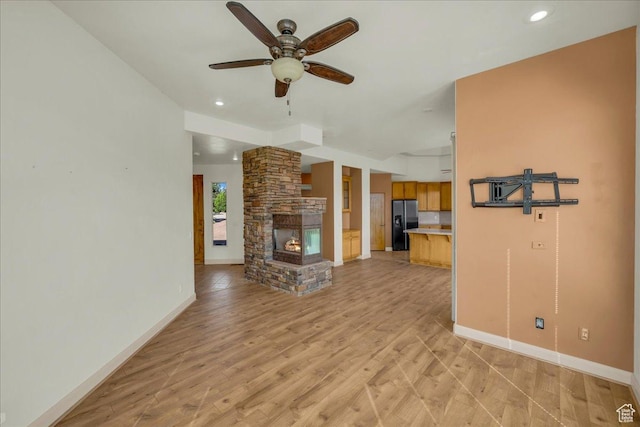 unfurnished living room with a ceiling fan, a stone fireplace, recessed lighting, light wood finished floors, and baseboards