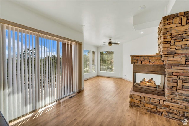 unfurnished living room featuring visible vents, baseboards, a stone fireplace, ceiling fan, and wood finished floors