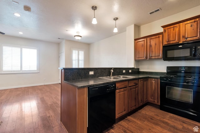 kitchen with visible vents, black appliances, a sink, dark countertops, and brown cabinets